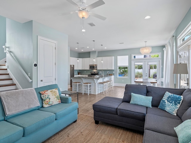 living room featuring hardwood / wood-style floors, sink, french doors, and ceiling fan with notable chandelier