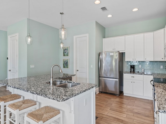 kitchen featuring sink, backsplash, light wood-type flooring, hanging light fixtures, and stainless steel fridge