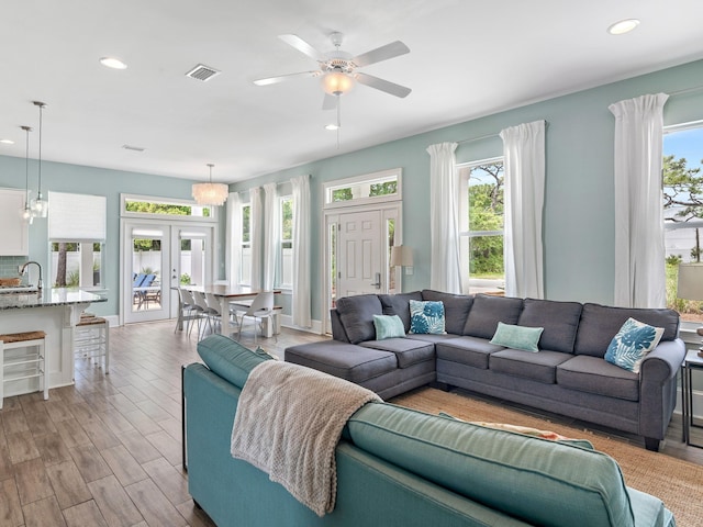 living room with ceiling fan with notable chandelier, wood-type flooring, french doors, and sink