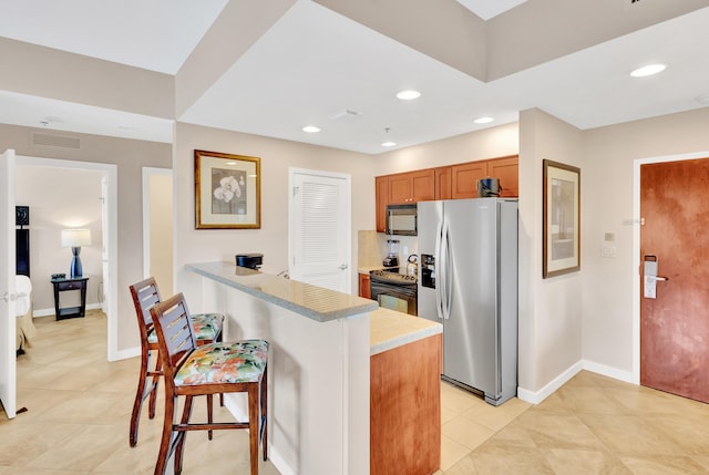 kitchen with kitchen peninsula, light tile flooring, a breakfast bar area, and black appliances