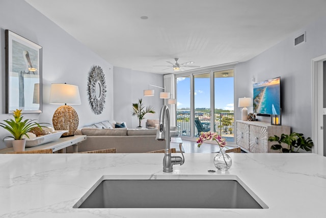 kitchen with floor to ceiling windows, sink, ceiling fan, and light stone countertops