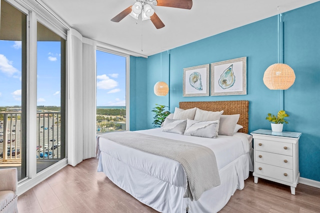 bedroom featuring hardwood / wood-style flooring, ceiling fan, access to outside, and a wall of windows