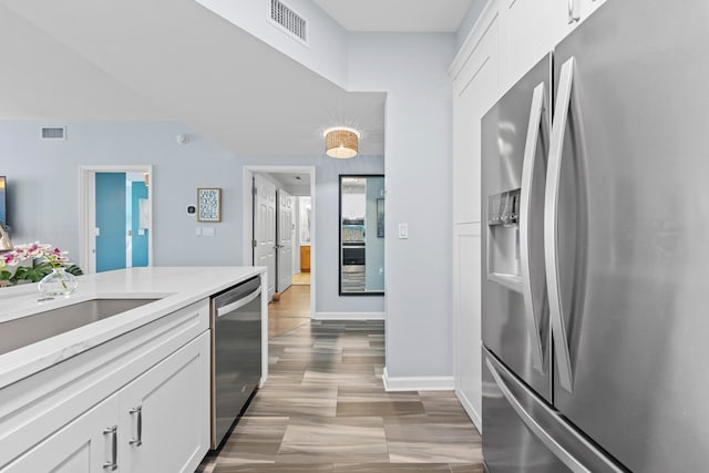 kitchen featuring white cabinets, stainless steel appliances, sink, light stone counters, and light hardwood / wood-style floors