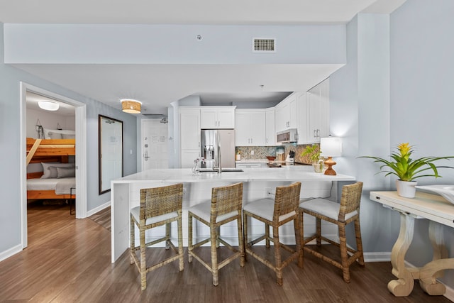 kitchen featuring white cabinets, tasteful backsplash, hardwood / wood-style floors, stainless steel fridge, and kitchen peninsula