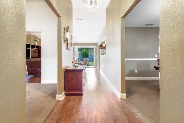 corridor with visible vents, a textured wall, wood finished floors, and a chandelier