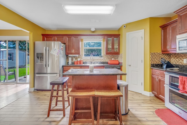 kitchen with decorative backsplash, a center island, a sink, light wood-style flooring, and appliances with stainless steel finishes