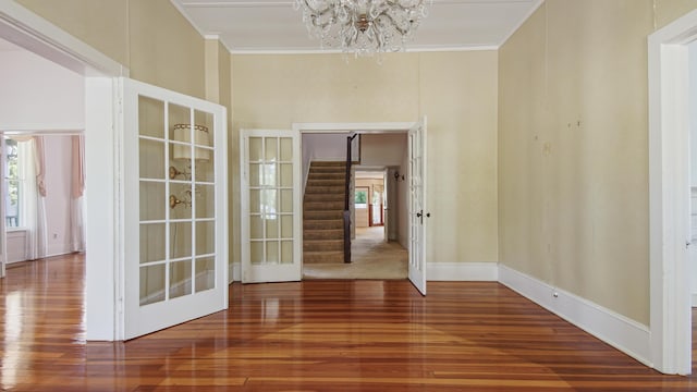 spare room with a notable chandelier, crown molding, wood-type flooring, and french doors