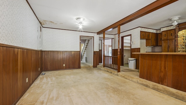 unfurnished living room with light colored carpet, ornamental molding, and wood walls