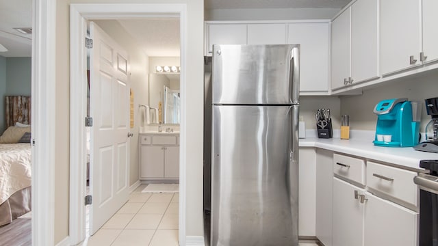 kitchen with white cabinets, stove, stainless steel fridge, and light tile floors