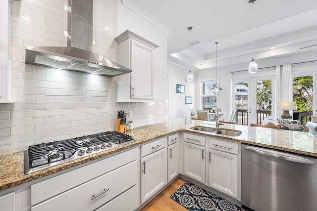 kitchen with wall chimney exhaust hood, tasteful backsplash, hanging light fixtures, stainless steel appliances, and light hardwood / wood-style flooring