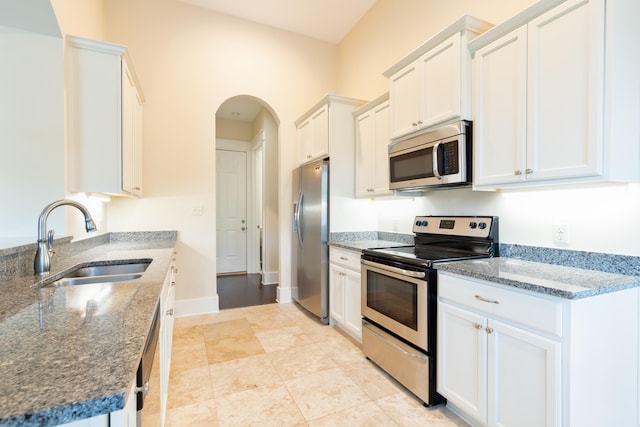 kitchen featuring white cabinetry, appliances with stainless steel finishes, light tile floors, sink, and dark stone counters