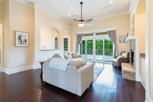 living room with ceiling fan, crown molding, a stone fireplace, and dark hardwood / wood-style floors