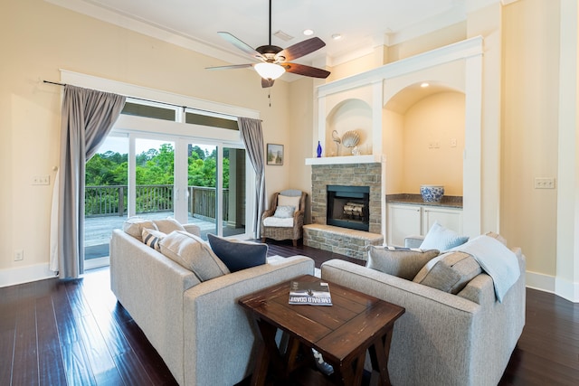 living room with ornamental molding, ceiling fan, a stone fireplace, and dark wood-type flooring