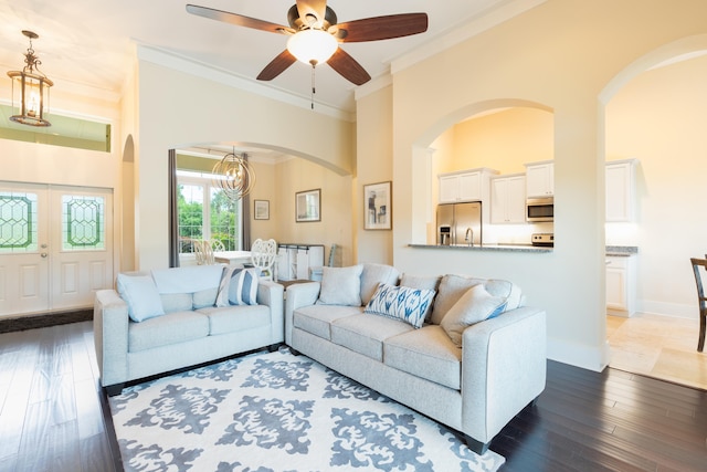 living room featuring ceiling fan with notable chandelier, ornamental molding, and dark wood-type flooring