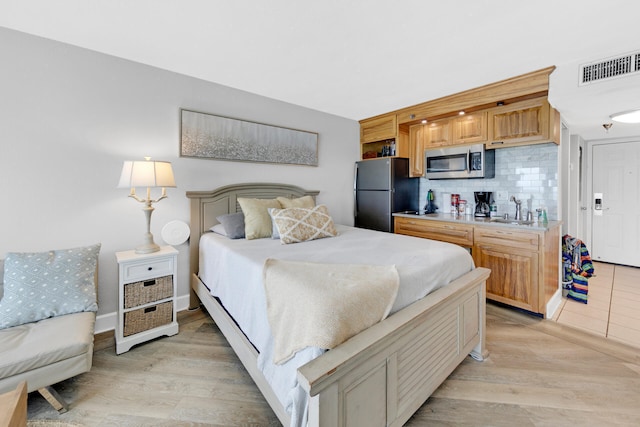 bedroom featuring stainless steel fridge, sink, and light hardwood / wood-style flooring