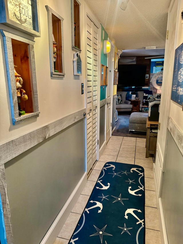 hallway with a textured ceiling and light tile floors