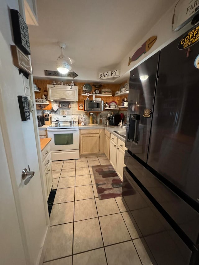 kitchen featuring sink, light tile floors, black fridge, and white range with electric cooktop