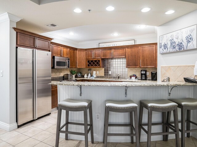 kitchen with appliances with stainless steel finishes, backsplash, light tile floors, and light stone countertops