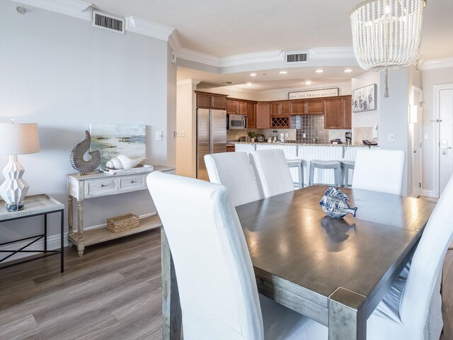 dining room with ornamental molding, wood-type flooring, and an inviting chandelier