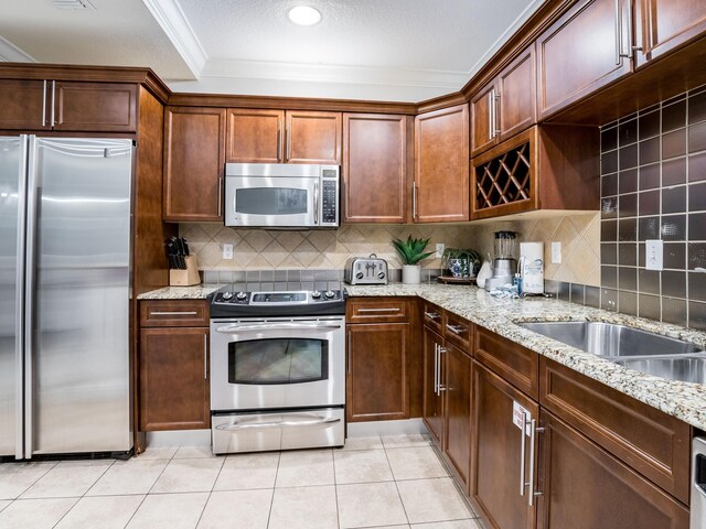 kitchen with appliances with stainless steel finishes, crown molding, tasteful backsplash, light stone counters, and light tile floors