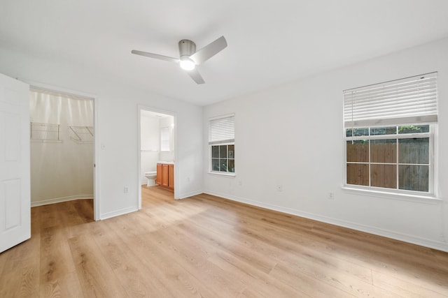 unfurnished bedroom with a closet, connected bathroom, ceiling fan, a walk in closet, and light hardwood / wood-style flooring