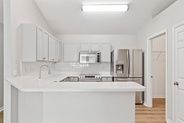 kitchen with stainless steel appliances, vaulted ceiling, light wood-type flooring, and kitchen peninsula