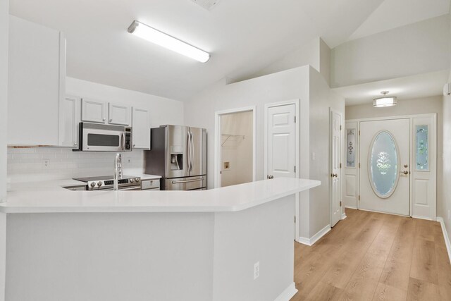 kitchen featuring appliances with stainless steel finishes, tasteful backsplash, vaulted ceiling, kitchen peninsula, and light hardwood / wood-style floors