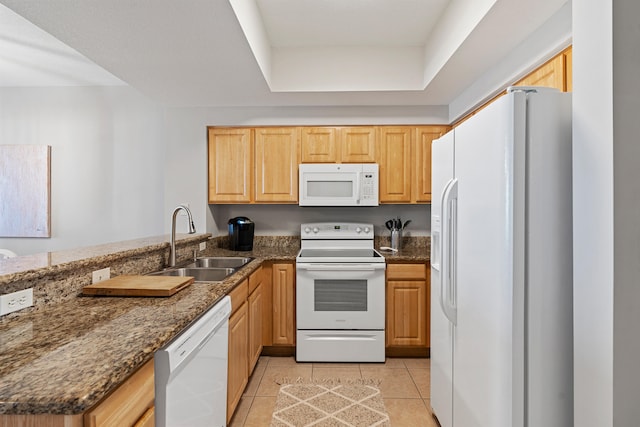 kitchen with dark stone counters, a tray ceiling, white appliances, light tile floors, and sink