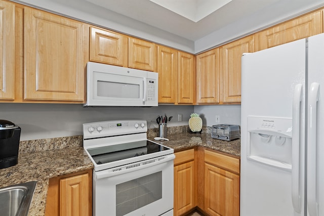 kitchen with white appliances, dark stone counters, and light brown cabinetry