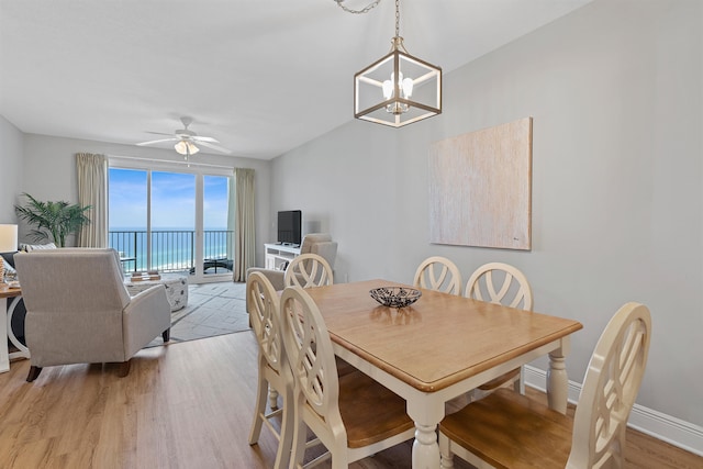 dining space with a water view, ceiling fan with notable chandelier, and hardwood / wood-style floors