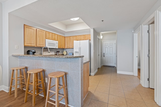 kitchen featuring light stone counters, kitchen peninsula, white appliances, light tile floors, and a breakfast bar