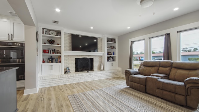 living room with light hardwood / wood-style floors, built in features, and a fireplace