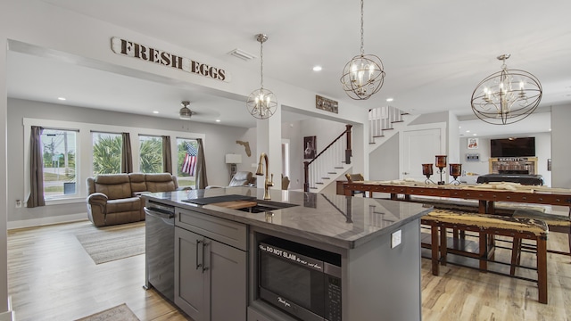 kitchen featuring a center island with sink, sink, ceiling fan, built in microwave, and decorative light fixtures