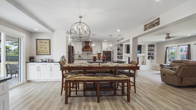 dining area featuring ceiling fan with notable chandelier, built in features, a fireplace, and light hardwood / wood-style flooring