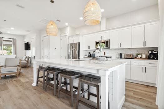 kitchen with appliances with stainless steel finishes, a kitchen island with sink, white cabinetry, and decorative light fixtures