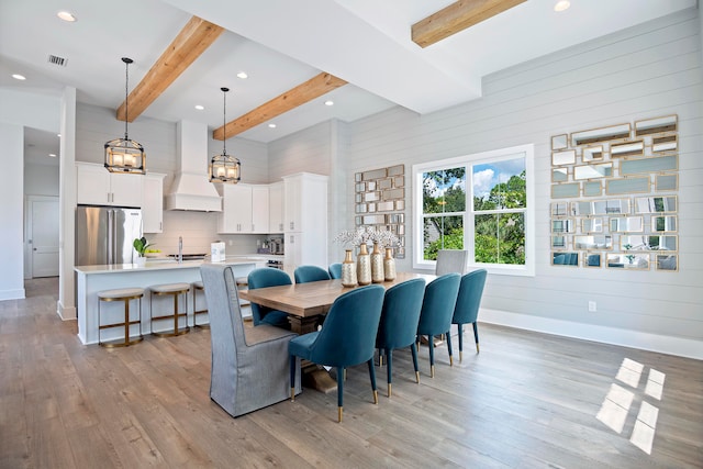 dining room with beamed ceiling, sink, and light hardwood / wood-style flooring