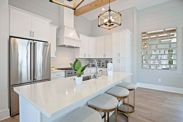 kitchen featuring beam ceiling, a center island with sink, decorative light fixtures, light wood-type flooring, and premium appliances