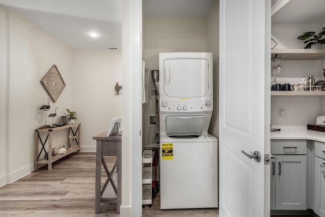 clothes washing area with light wood-style floors, laundry area, baseboards, and stacked washing maching and dryer