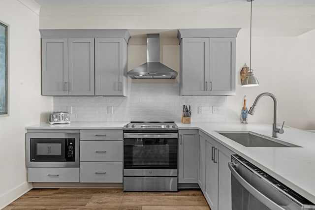 kitchen with wall chimney range hood, appliances with stainless steel finishes, gray cabinets, and a sink