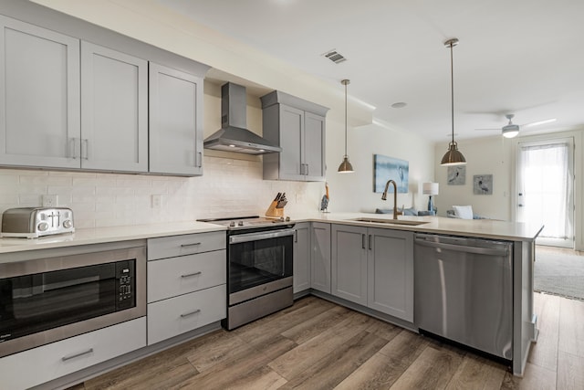 kitchen featuring wall chimney range hood, appliances with stainless steel finishes, gray cabinets, and a sink