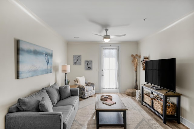 living room with ceiling fan, crown molding, baseboards, and wood finished floors