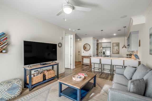 living room featuring light wood-type flooring, ceiling fan, baseboards, and crown molding