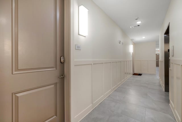 hallway with visible vents, a decorative wall, and wainscoting