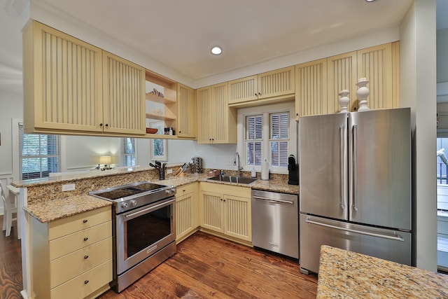 kitchen featuring kitchen peninsula, stainless steel appliances, dark hardwood / wood-style flooring, light stone counters, and sink