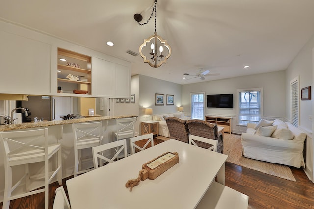 dining room with ceiling fan with notable chandelier, sink, and dark wood-type flooring