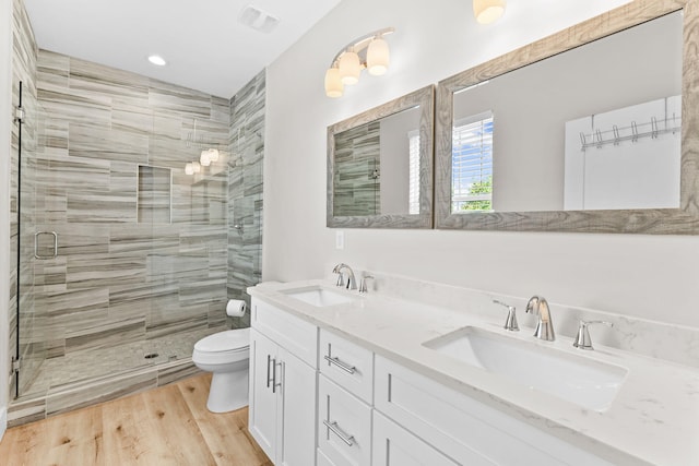 bathroom featuring a shower with shower door, hardwood / wood-style flooring, large vanity, toilet, and dual sinks