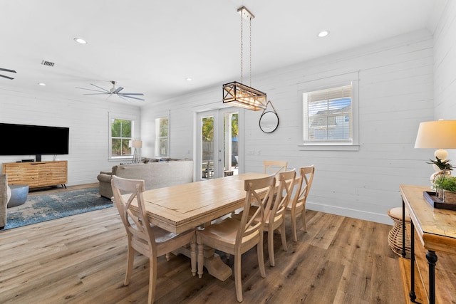 dining room featuring wood-type flooring, wooden walls, ceiling fan, and french doors