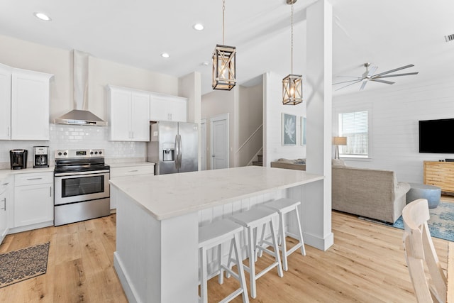 kitchen featuring appliances with stainless steel finishes, wall chimney exhaust hood, light hardwood / wood-style flooring, and pendant lighting