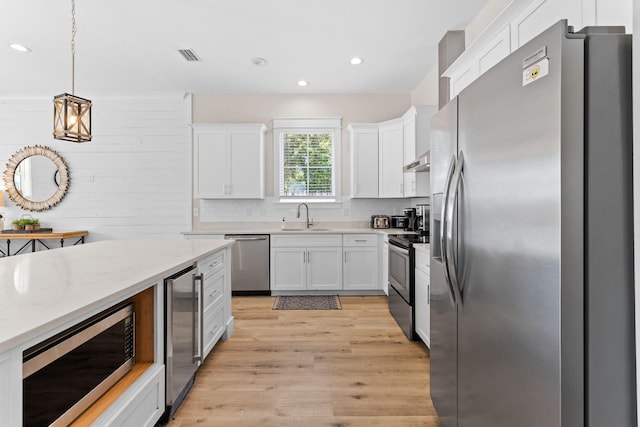 kitchen with appliances with stainless steel finishes, light hardwood / wood-style floors, white cabinetry, and pendant lighting