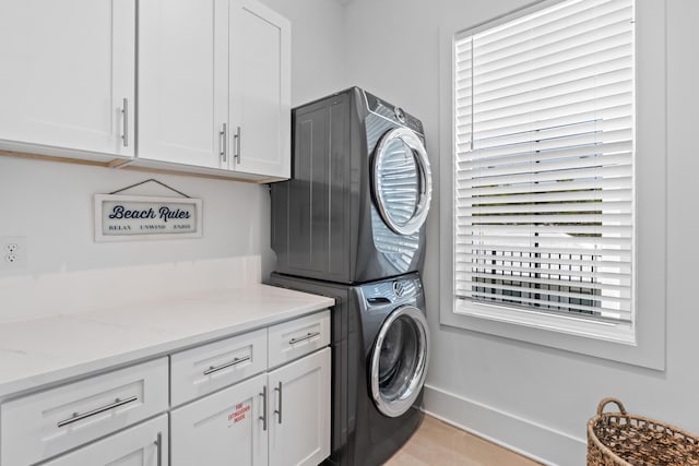 clothes washing area with stacked washing maching and dryer, cabinets, and light hardwood / wood-style flooring